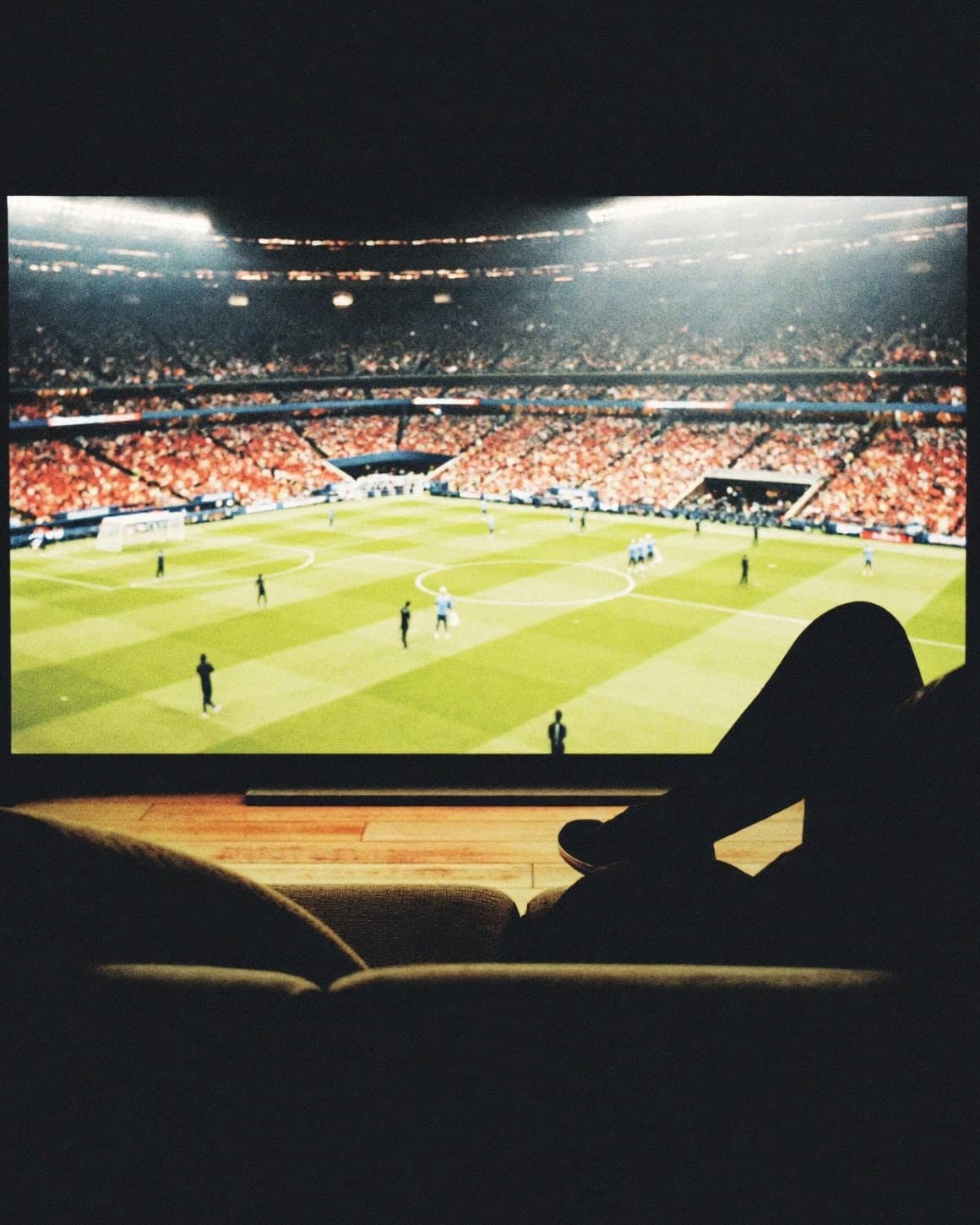 A living room at night lit only by a large television showing a floodlit football match