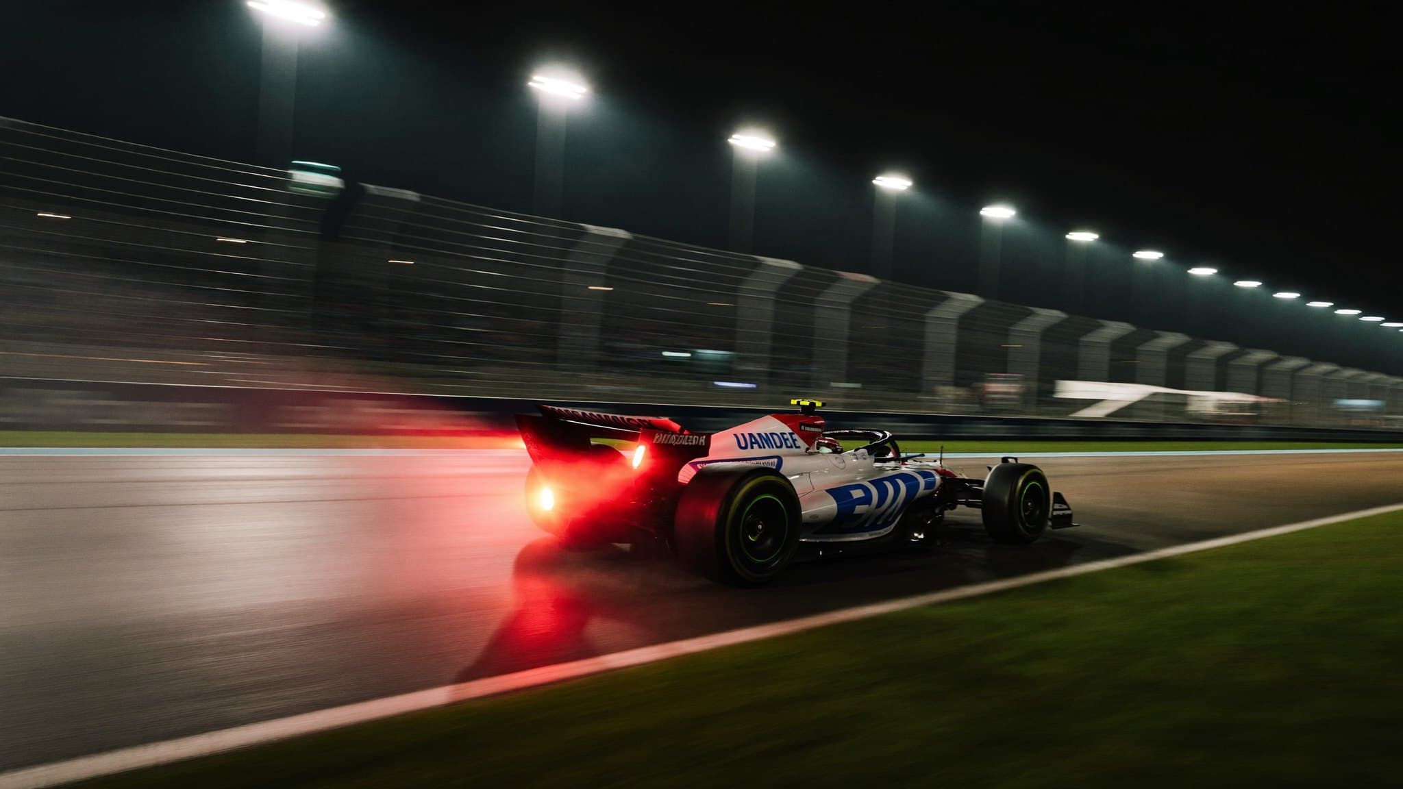 A racing car cornering under floodlights on a wet circuit at night
