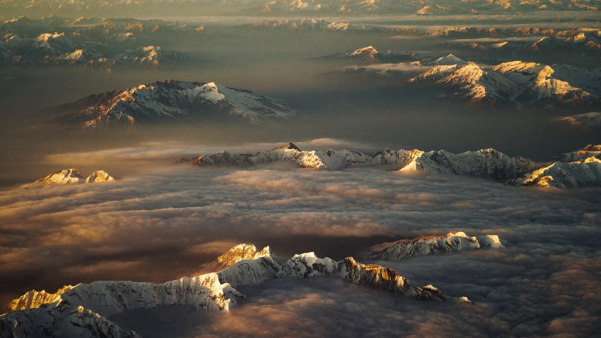 Aerial view of a snow capped mountain range above a sea of cloud at golden hour